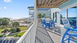 Ein Balkon mit Blick auf den Strand, blaue Stühle und ein Holzdeck.