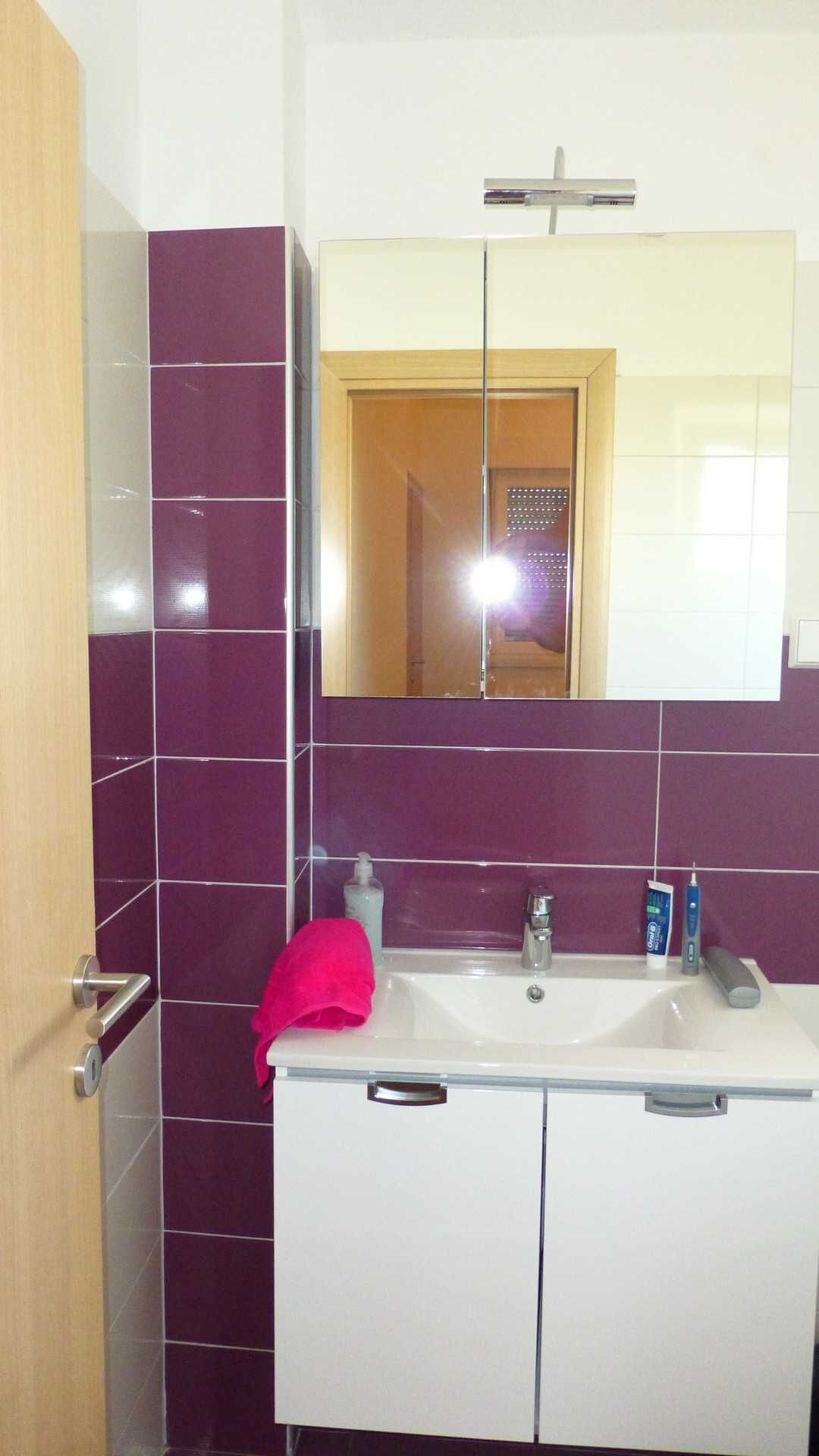 A bathroom with purple tiles, a white sink, a mirror, and a door.