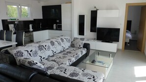 A modern living room with a sofa, a coffee table, a TV, and a kitchen area with cabinets and appliances. - Apartment Barbara  in Okrug Gornji (Okrug Gornji)