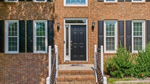 A two-story brick building with a central black door, white-framed windows, and a small porch with a metal railing. - Near Downtown Cary and Raleigh - 5 room King beds, walking distance to Bond Park (Cary)