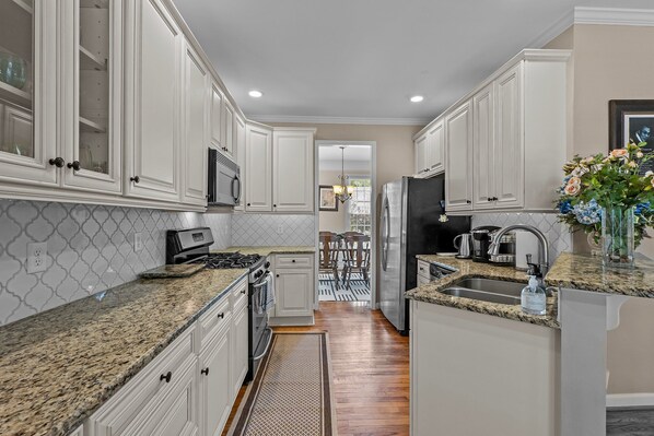 A kitchen with white cabinets, granite countertops, stainless steel appliances, and a view into the dining area.