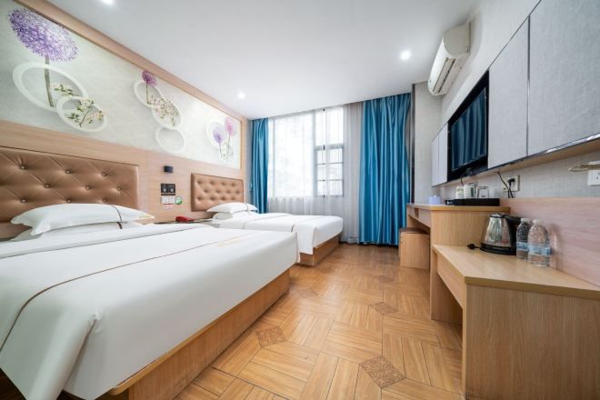 A hotel room with two beds, a wooden floor, a TV, a desk, and a window with curtains.