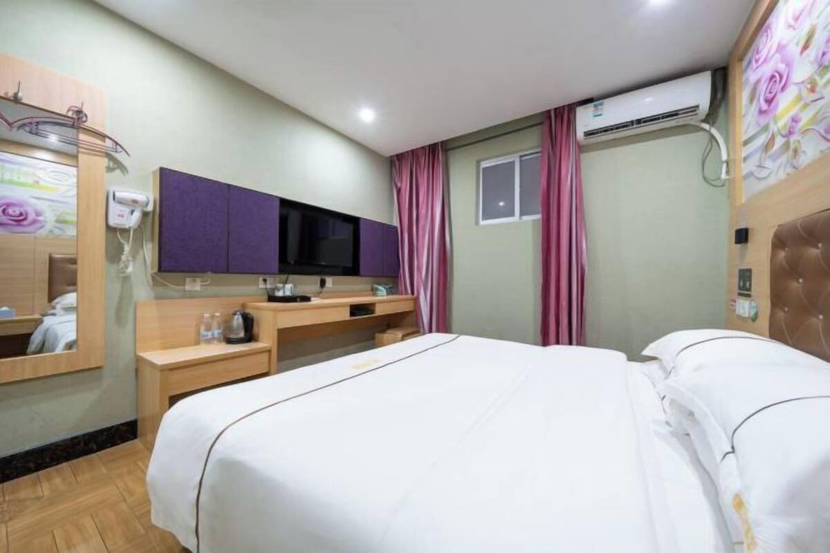 A hotel room with a bed, a desk, a television, and an air conditioning unit.