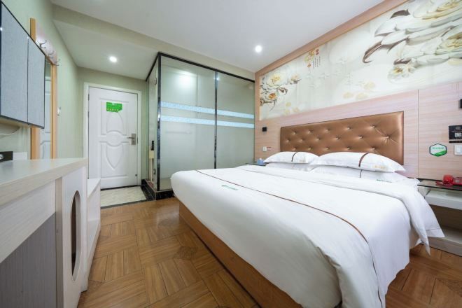 A hotel room with a large bed, a wooden floor, a bathroom with a glass shower, and a wall with a floral mural.