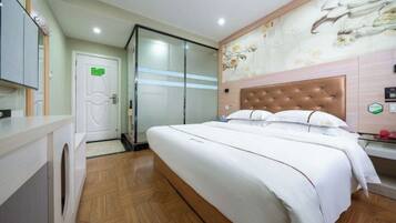 A hotel room with a large bed, a wooden floor, a bathroom with a glass shower, and a wall with a floral mural.