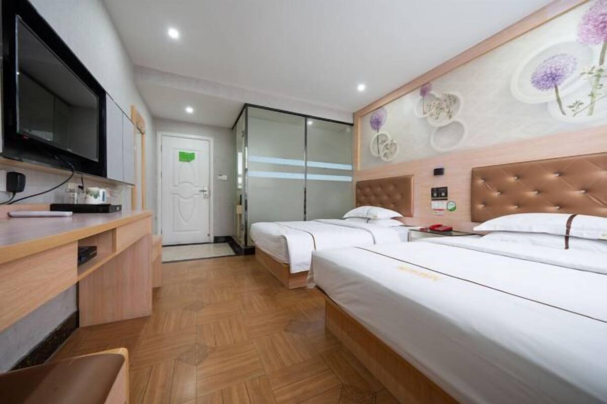A hotel room with a television, a desk, two beds, a mirror, and a door.