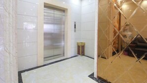 Un ascensor moderno con acabados metálicos, rodeado de paredes de azulejos blancos y un suelo de mármol.