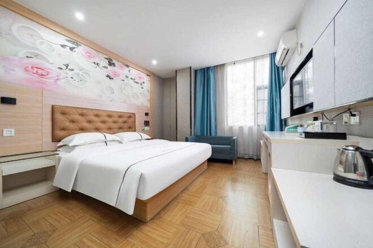 A modern hotel room with a large bed, a kitchenette, and a decorative wall.