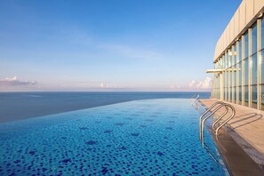 Piscina infinita con vistas despejadas al océano, barandilla de cristal y fachada moderna de edificio.