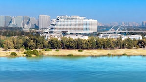 A modern hotel with a large, multi-story structure, surrounded by a park and a body of water.