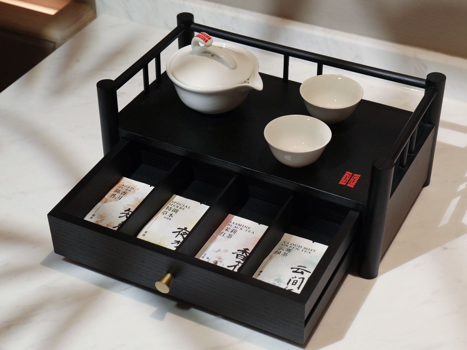 A black tray with a white teapot, two cups, and a box of tea bags.