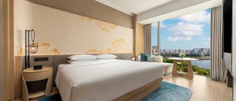 A modern hotel room with a large bed, a nightstand, a desk, and a view of a cityscape.