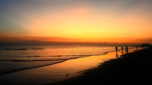 A beach at sunset with people walking along the shore.