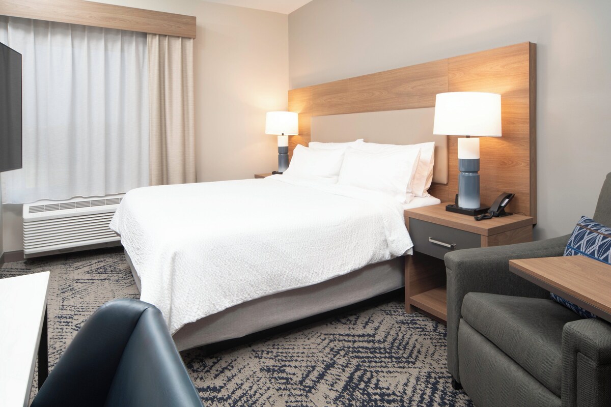 Habitación de hotel con cama, dos lámparas de noche, escritorio, silla, televisor y ventana con cortinas.