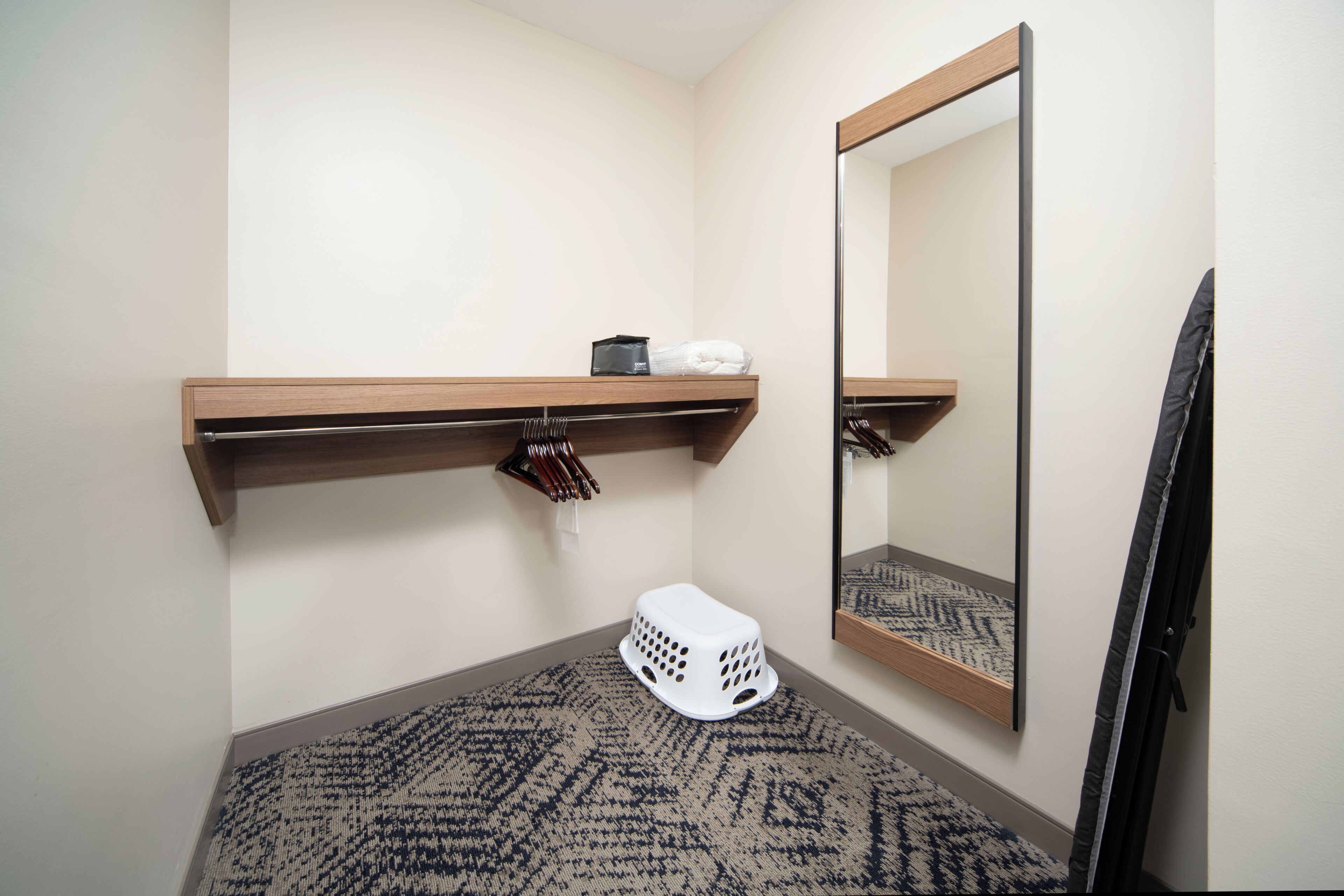 Un baño pequeño con un estante de madera, un espejo, un cesto de ropa blanca y un tapete estampado.