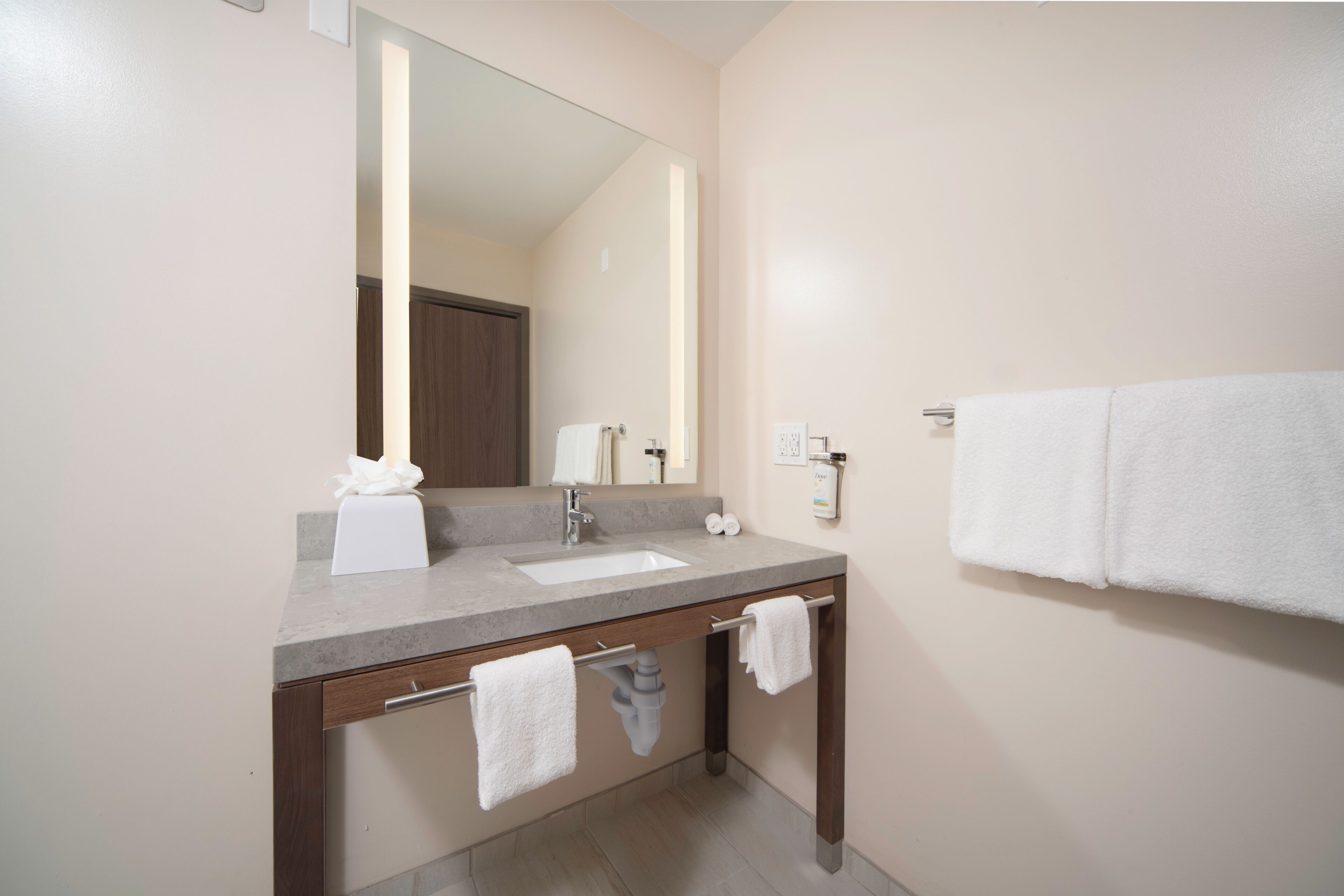 A bathroom with a sink, mirror, towel rack, and a towel dispenser.