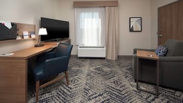 Une chambre d’hôtel équipée d’un bureau, d’une télévision, d’une chaise, d’un canapé, d’une petite table et d’une fenêtre avec des rideaux.