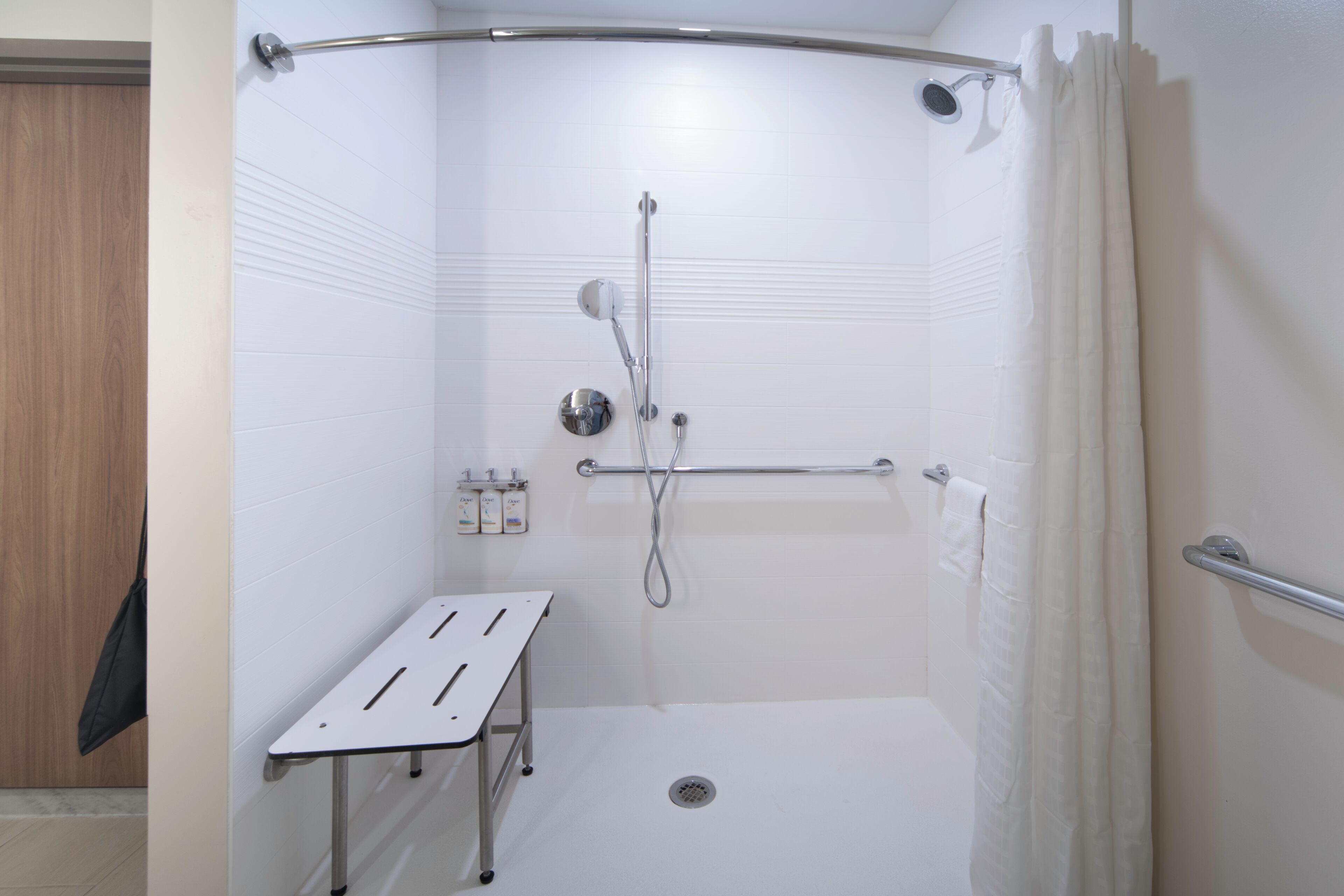 A modern shower area with a handheld showerhead, a handheld shower attachment, and a shower seat.
