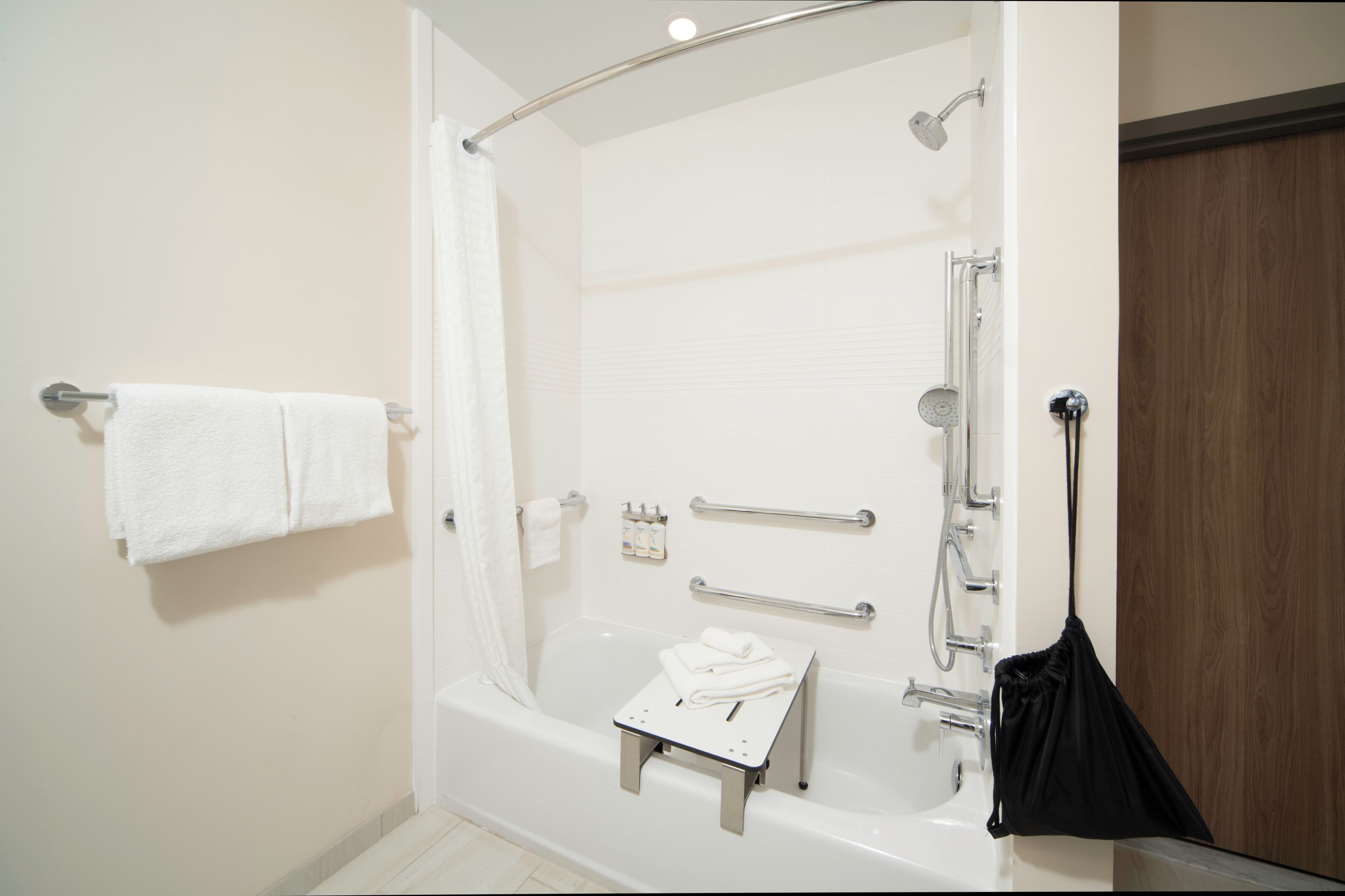 A modern bathroom with a bathtub, shower, and handrails.
