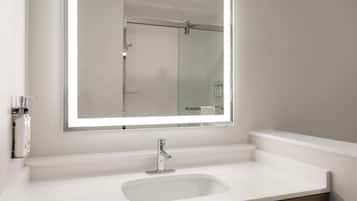 Une salle de bain avec un lavabo blanc, un miroir et une porte de douche.