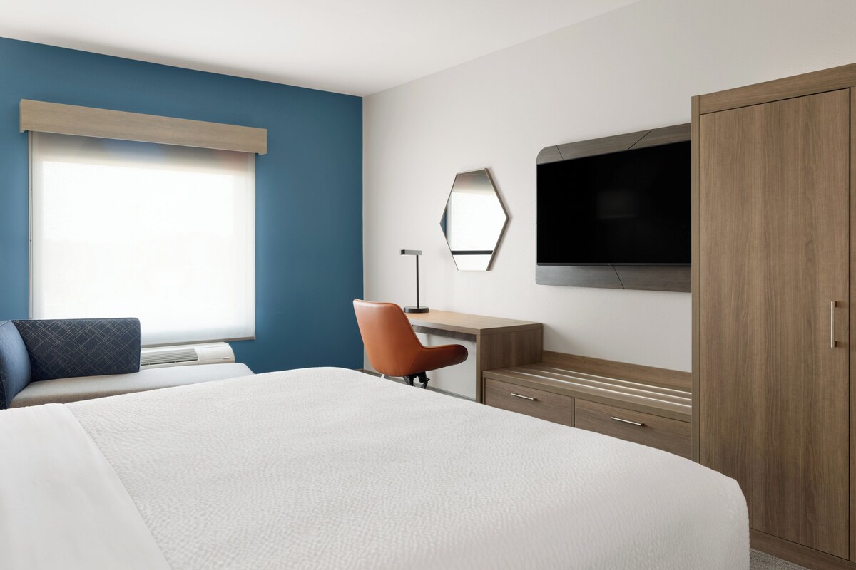 Una camera d'albergo con un letto grande, una scrivania con una sedia, una televisione e un armadio.