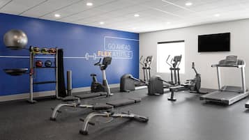 Ein modernes Fitnessstudio mit verschiedenen Trainingsgeräten, einer blauen Wand mit motivierenden Texten und einem großen Fenster.