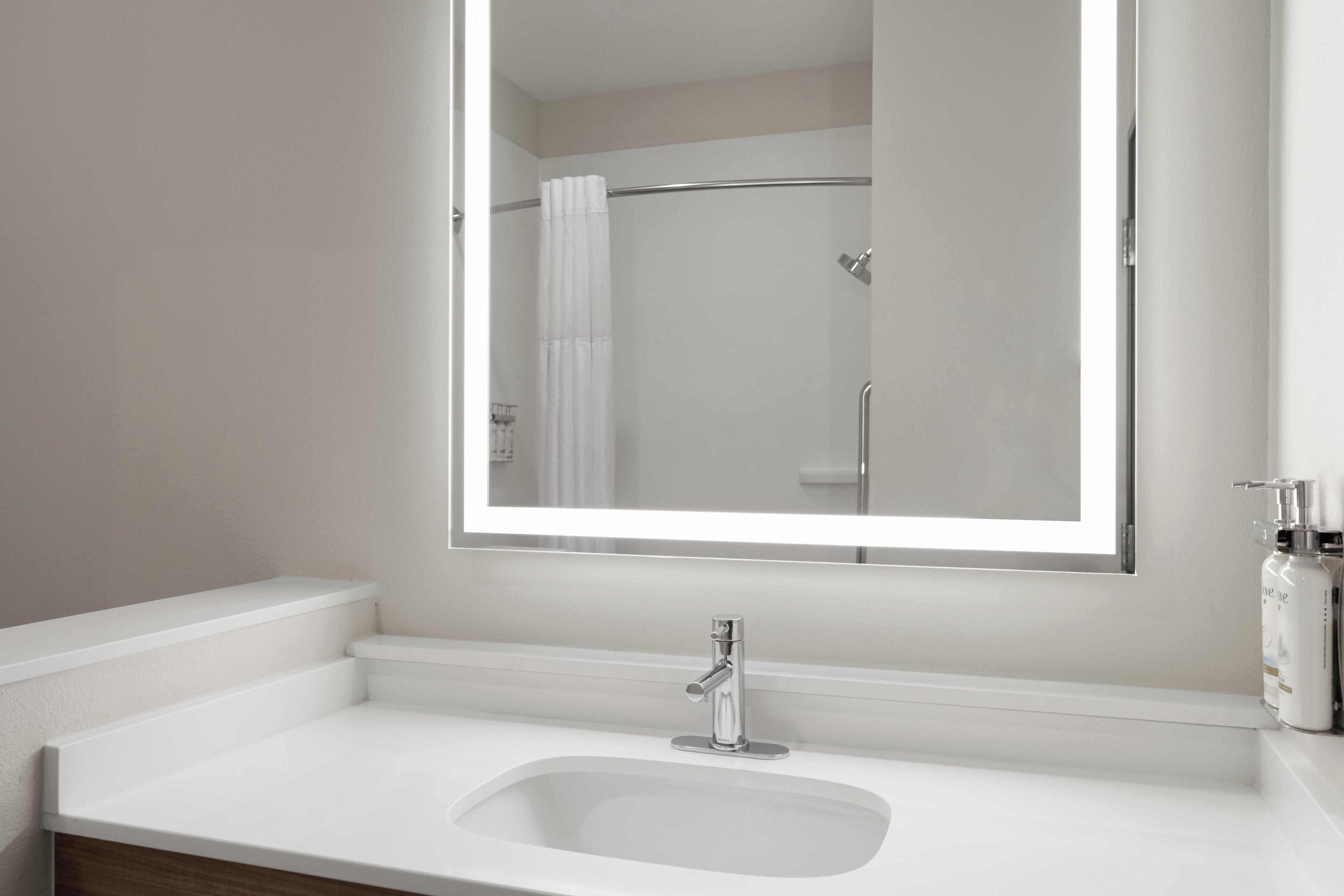 Un bagno con un lavandino bianco, uno specchio e una doccia visibile nel riflesso.