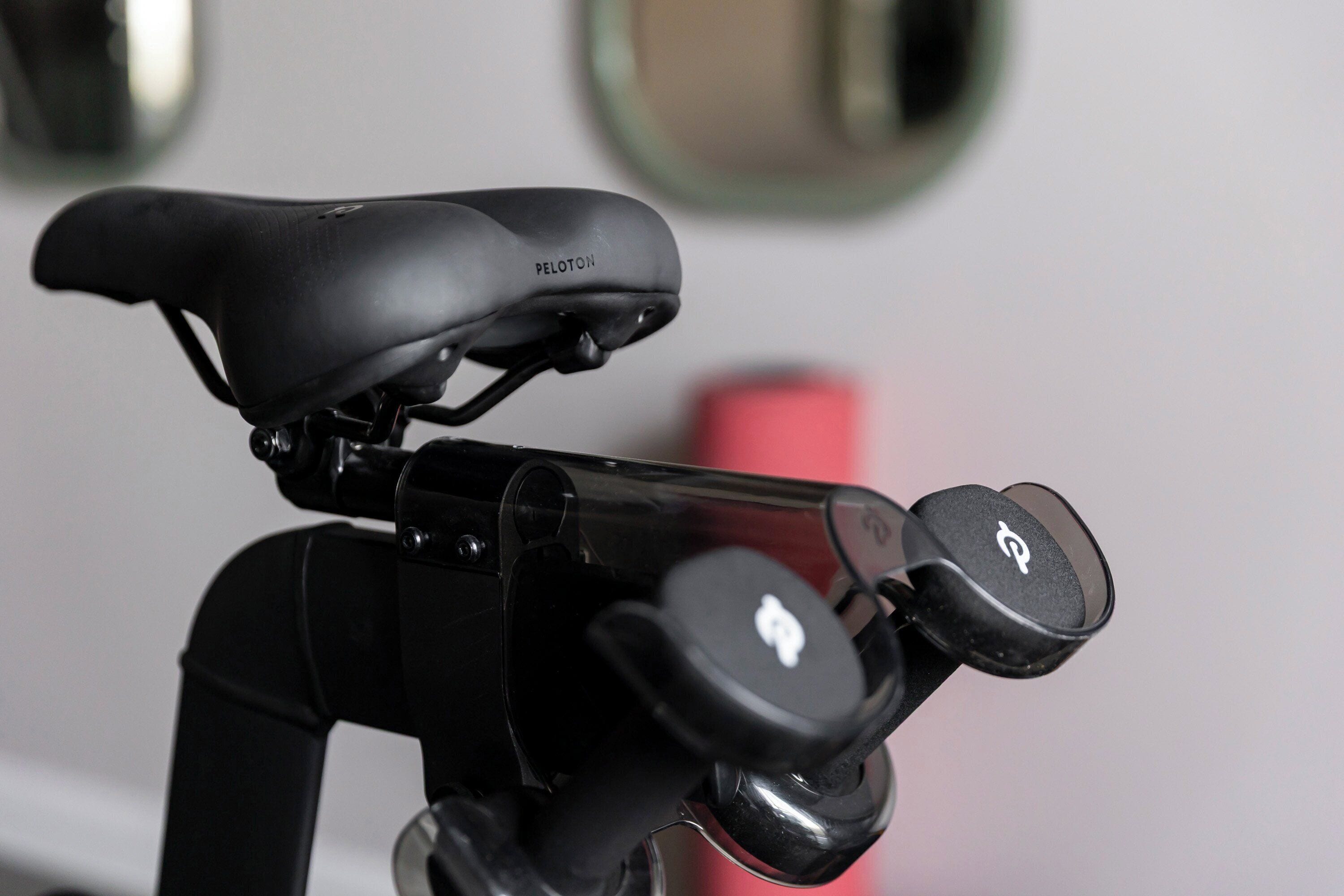 Ein Fahrrad mit schwarzem Sattel, beschriftet mit „PELOTON“, und einem Lenker mit einem Logo.