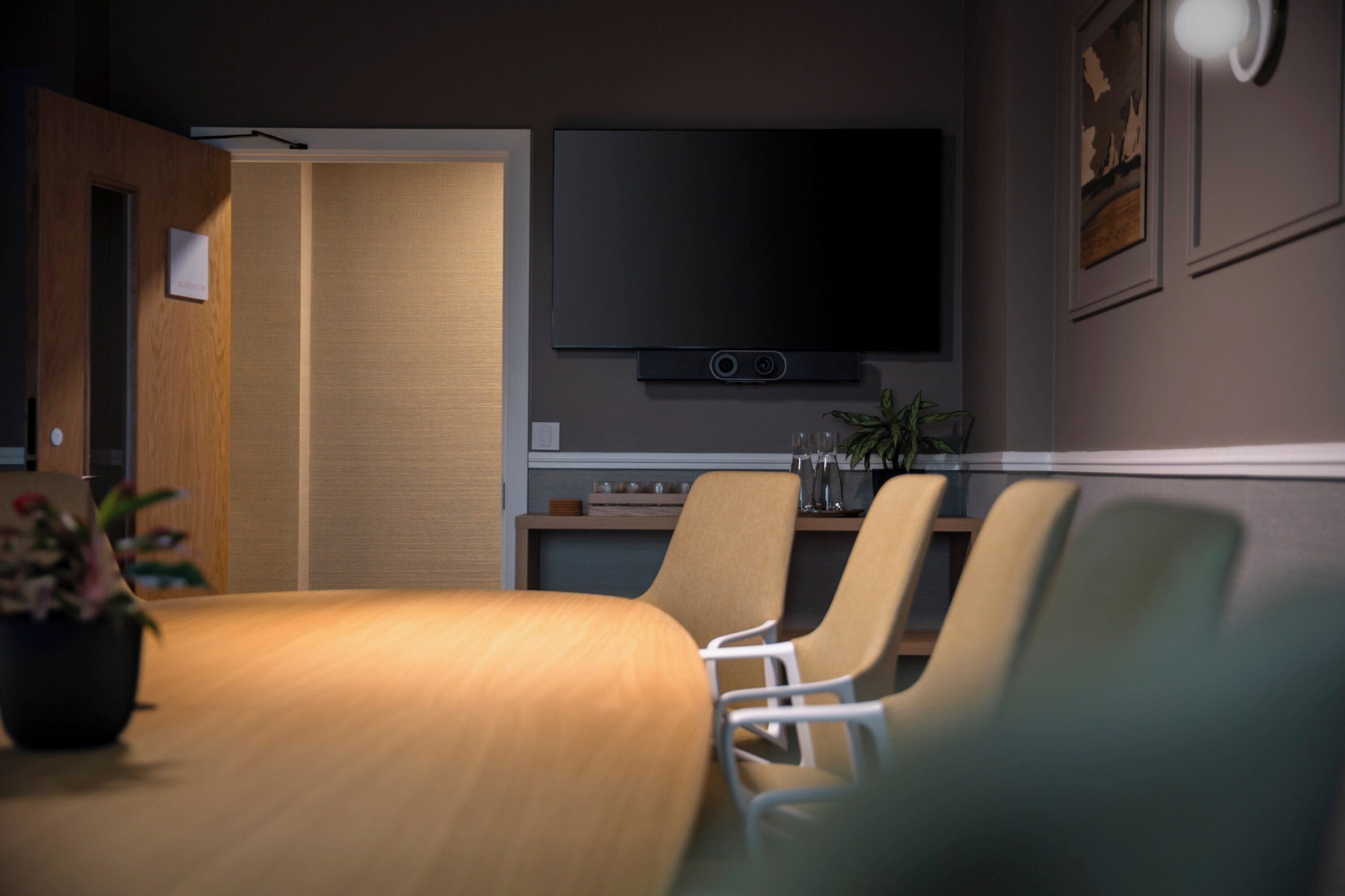 A conference room with a wooden table, four chairs, a flat-screen TV, and a small plant.
