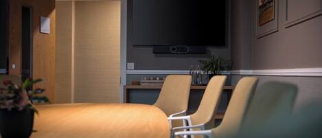 A conference room with a wooden table, four chairs, a flat-screen TV, and a small plant.