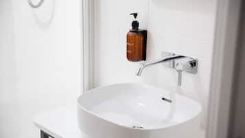 A white bathroom with a vessel sink, a handheld showerhead, and a soap dispenser on the wall.
