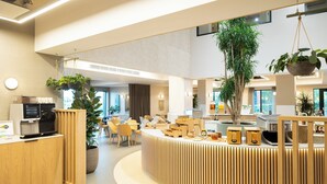 A modern reception area with a wooden counter, seating area, and large potted plants. - voco Zeal Exeter Science Park by IHG (Exeter)