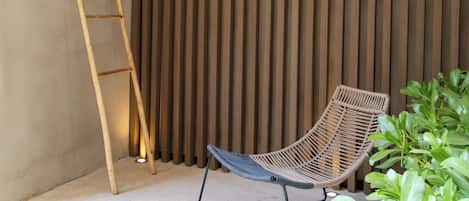 A corner with a wooden slatted wall, a wicker chair, a wooden ladder, and a potted plant.