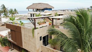 Una terraza en la azotea con piscina, plantas en macetas y una estructura de techo de paja.