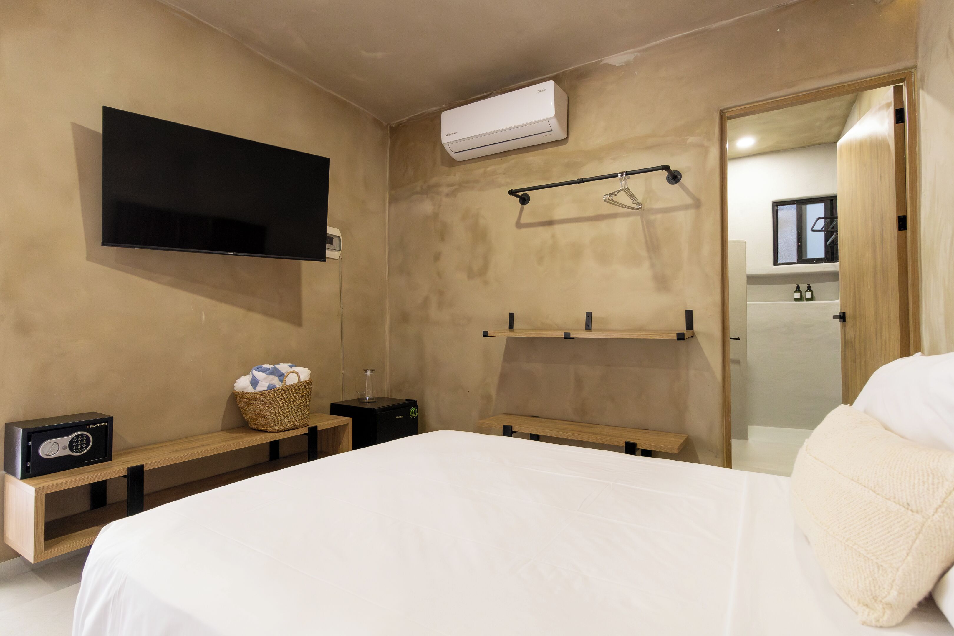 A modern bedroom with a bed, a TV mounted on the wall, a small bedside table with a radio, and a wall-mounted air conditioner.