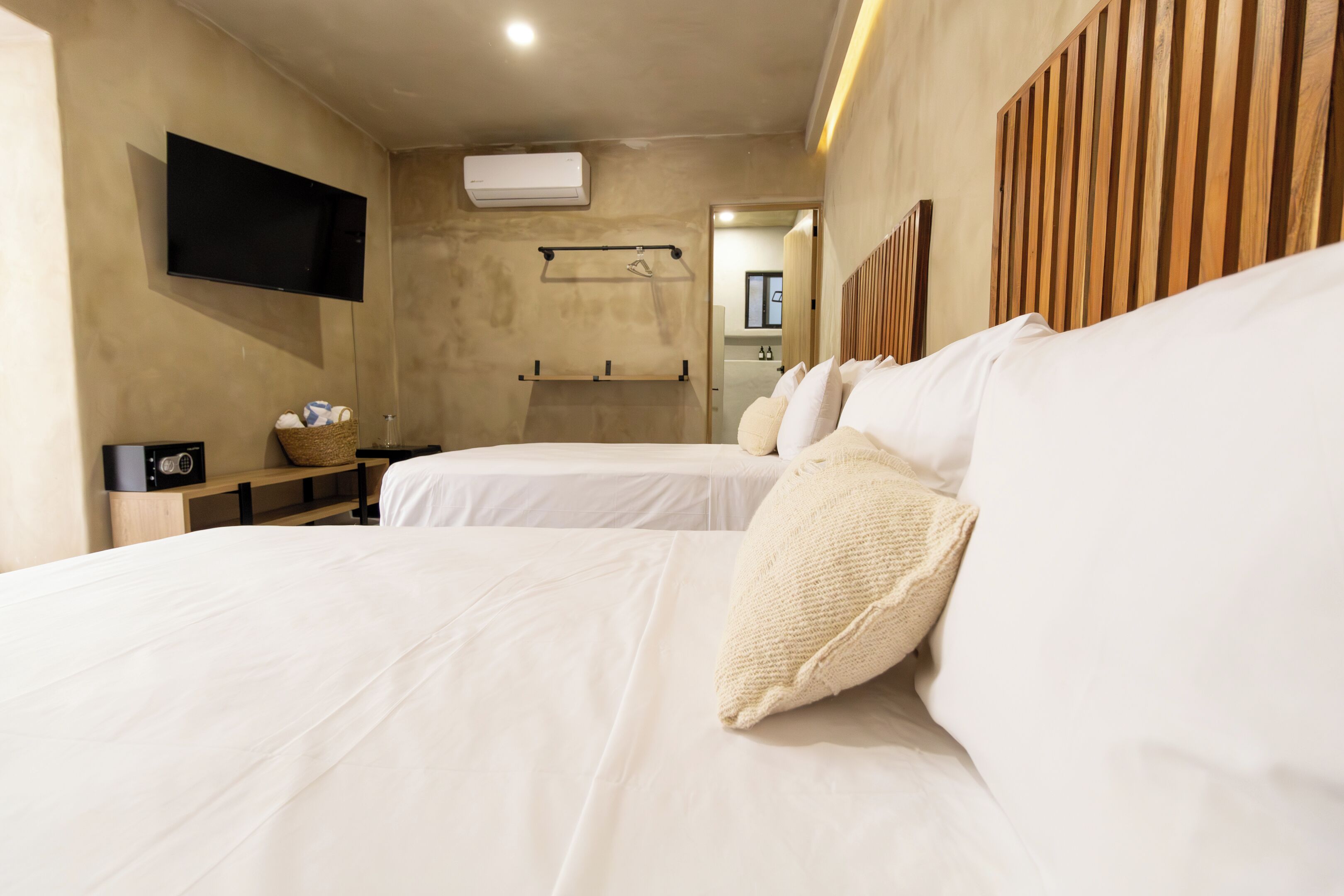 A hotel room with two beds, a flat-screen TV, an air conditioning unit, and a wooden headboard.