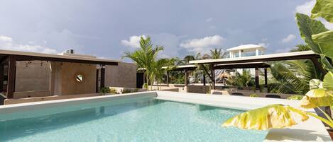 A clear swimming pool with a modern architectural design, surrounded by palm trees and a clear sky.