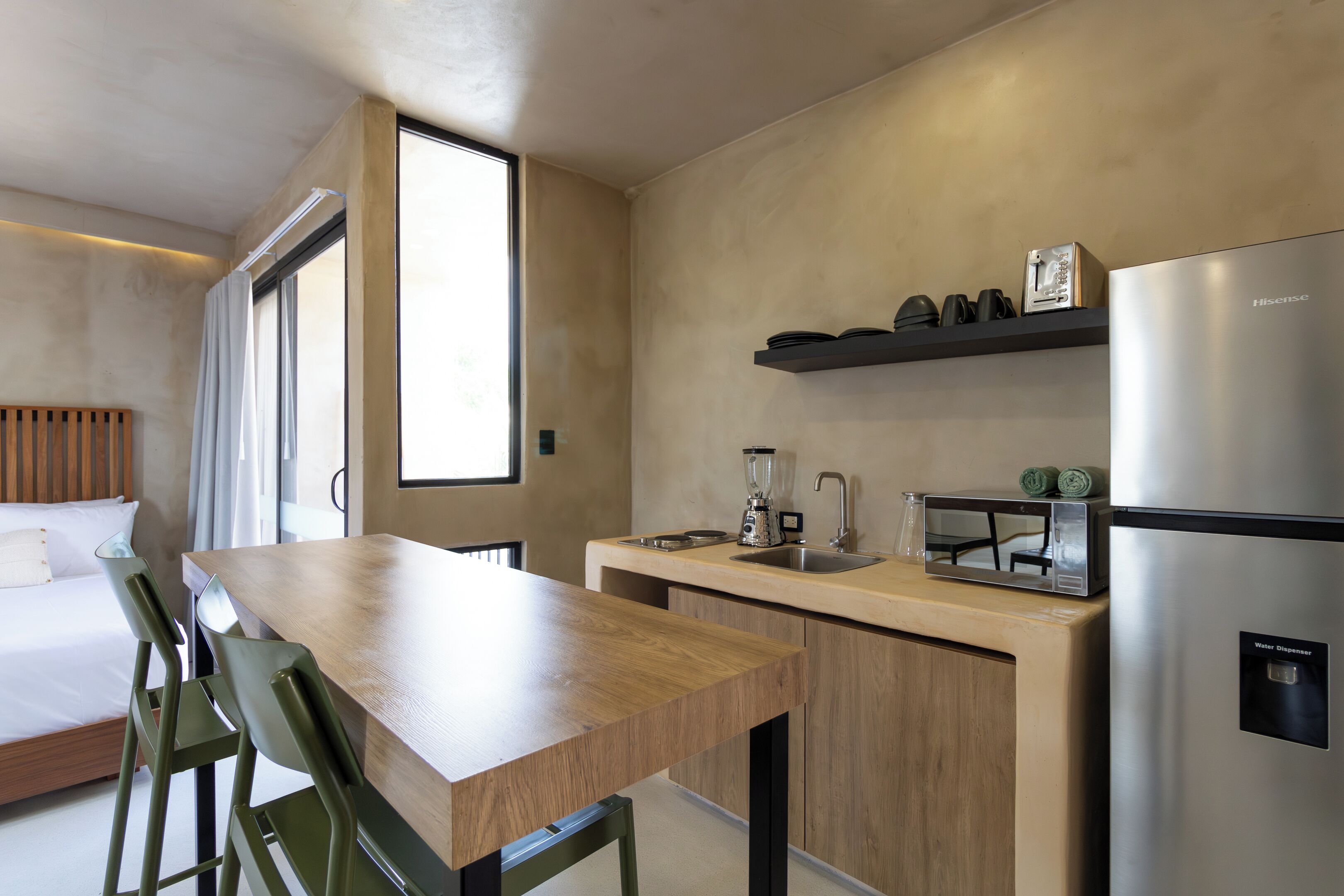 Une cuisine moderne avec une table en bois, des tabourets de bar, un four encastré et un distributeur d’eau.
