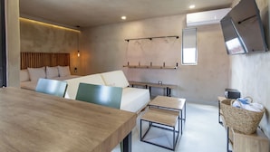 Ein modernes, minimalistisches Zimmer mit einem Holzesstisch, einer Couch mit Kissen, einem kleinen Fernseher und einem Wand-Fernseher.