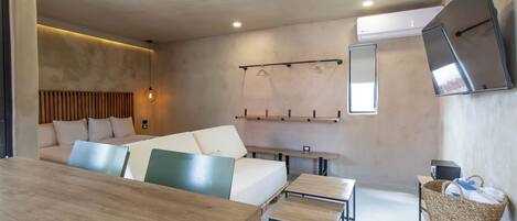 A modern, minimalist room with a wooden dining table, a sofa with cushions, a small TV, and a wall-mounted TV.