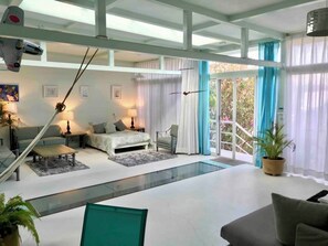 A spacious living area with a large bed, a sofa, and a dining table. There is a staircase leading to an outdoor area with a view of trees. - 2nd FL high ceiling loft with pool (Oaxaca de Juárez)