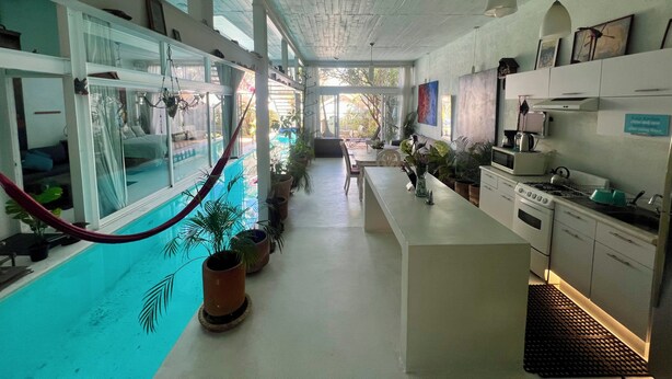 A spacious kitchen with a central island, a dining area, and a pool area visible through glass doors. - Two story high ceiling loft with heated pool (Oaxaca de Juárez)