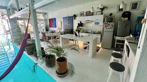 A modern kitchen with white cabinets, a dining area with a table and chairs, and a pool area with a hammock. - Two story high ceiling loft with heated pool (Oaxaca de Juárez)