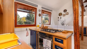 A kitchen with wooden cabinets, a gas stove, an oven, and a window with a view of trees. - Awesome apartment in Ravna Gora with WiFi (Ravna Gora)