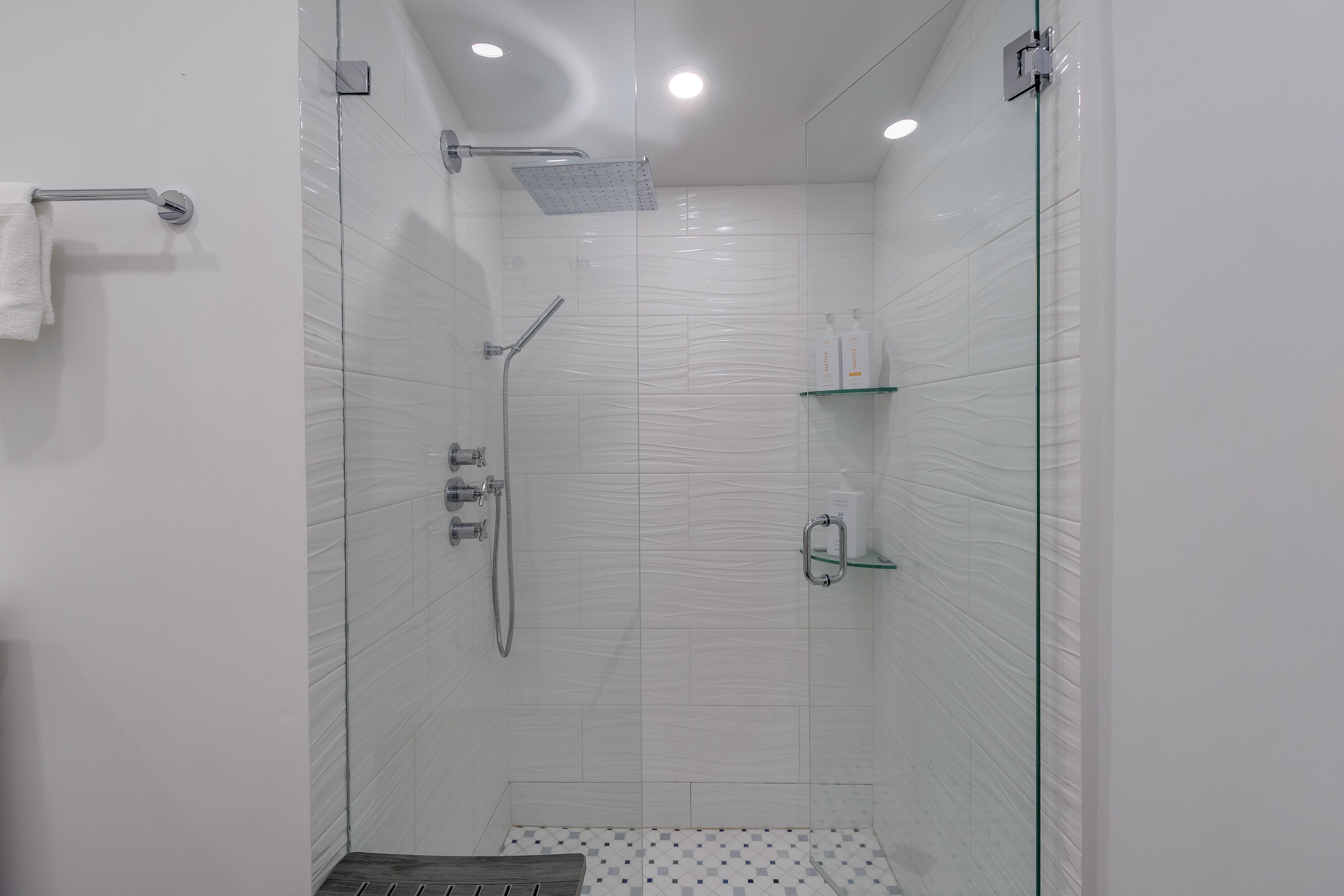 Una ducha moderna con puerta de cristal, cabezal de ducha de mano y grifo empotrado.