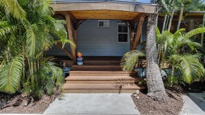Ein Haus mit einer Holzveranda, Treppen zum Eingang und üppigen Palmen rund um das Grundstück.