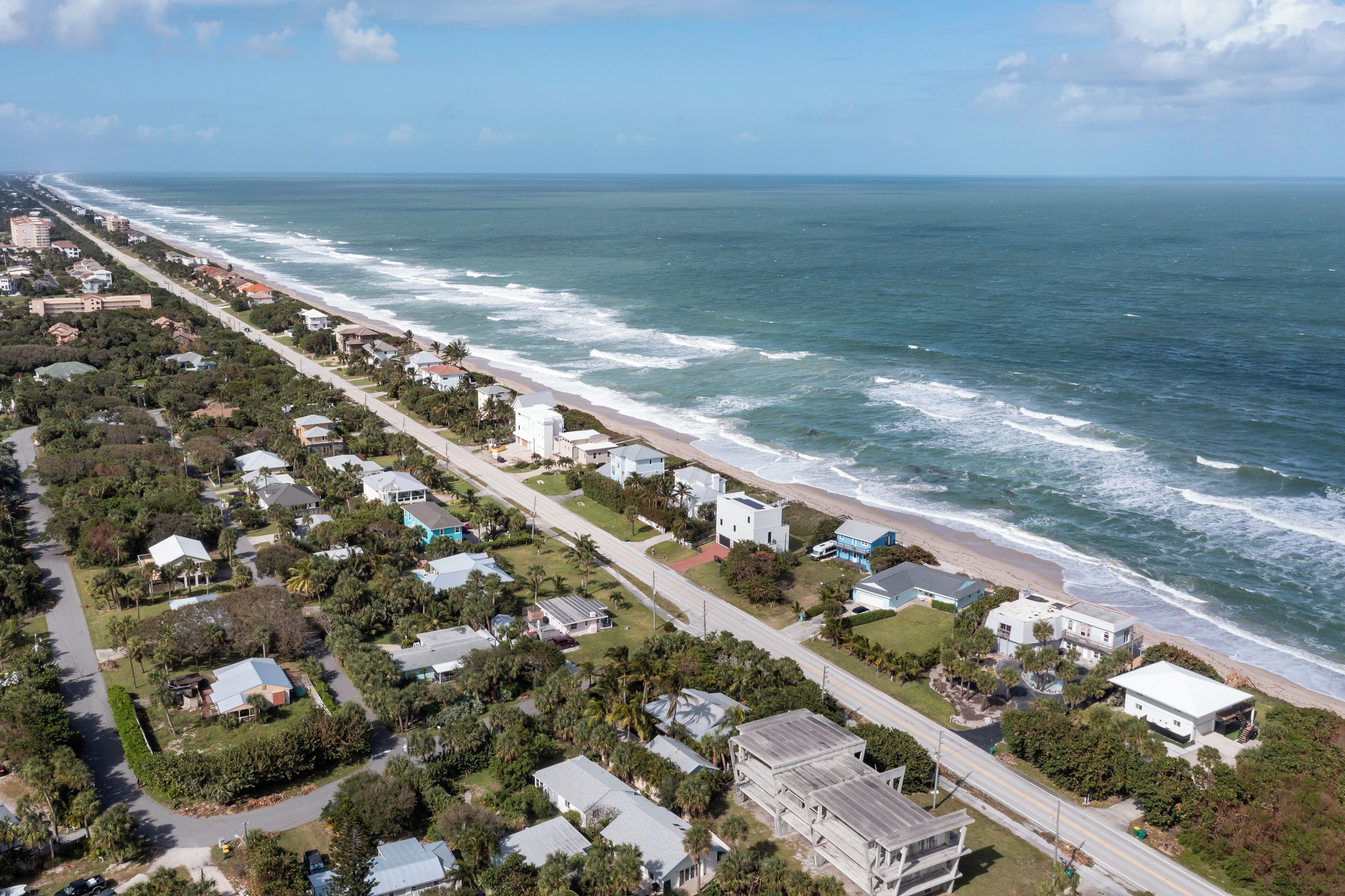 Luftaufnahme einer Küstenwohngegend mit Häusern, einer Straße und einem Strand.
