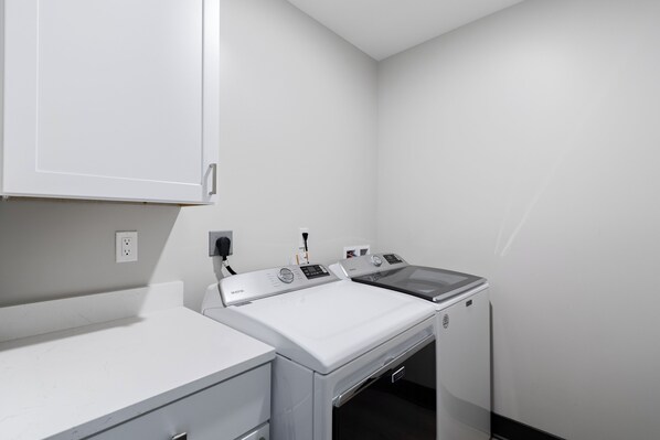 A laundry room with a white washing machine and dryer, a countertop, and a cabinet.