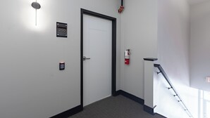 A hallway with a door, a fire alarm, and a staircase.