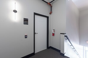 A hallway with a door, a fire alarm, and a staircase. - Modern 2-bedroom apartment in the middle of Downtown Janesville! (Janesville)